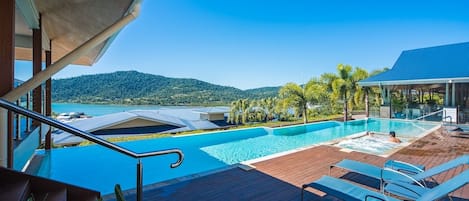 Zona de piscina con deck de madera, sillas de descanso y vista a un paisaje natural.
