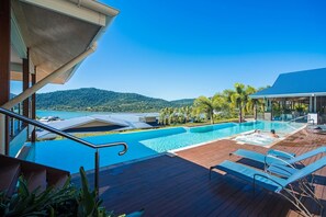 A pool area with a wooden deck, lounge chairs, and a view of a natural landscape.