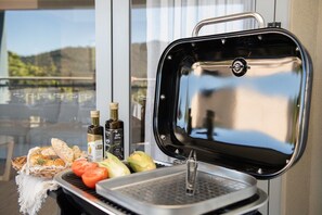 A portable grill with a basket of bread and vegetables, and two bottles of olive oil. - Villa Luxe On Airlie (Airlie Beach)