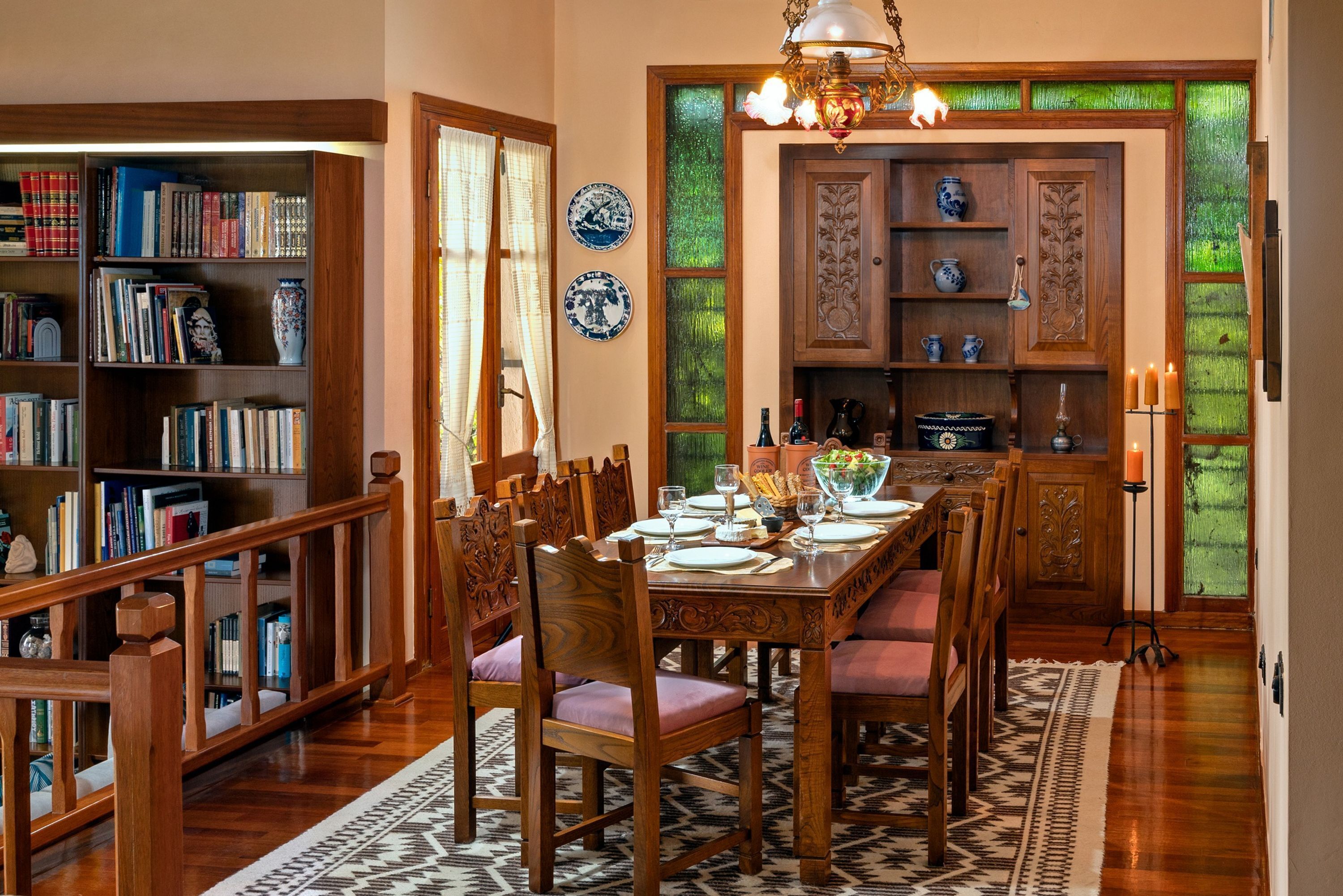 Un coin repas avec une table en bois dressée pour quatre personnes, entourée de chaises, et une bibliothèque remplie de livres et d’objets décoratifs.