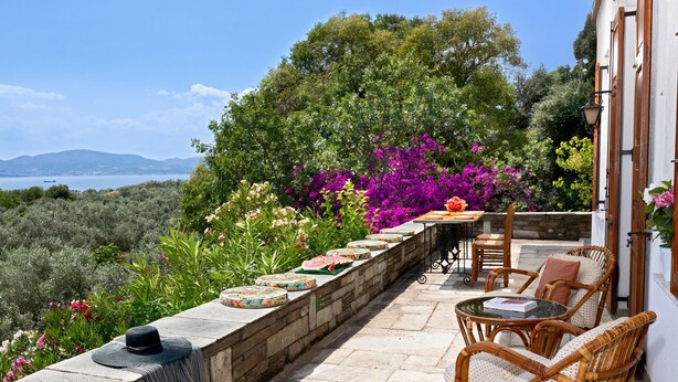 A terrace with wicker furniture, a stone wall, and a view of the sea. - Villa Annelies Pelion (Volos)