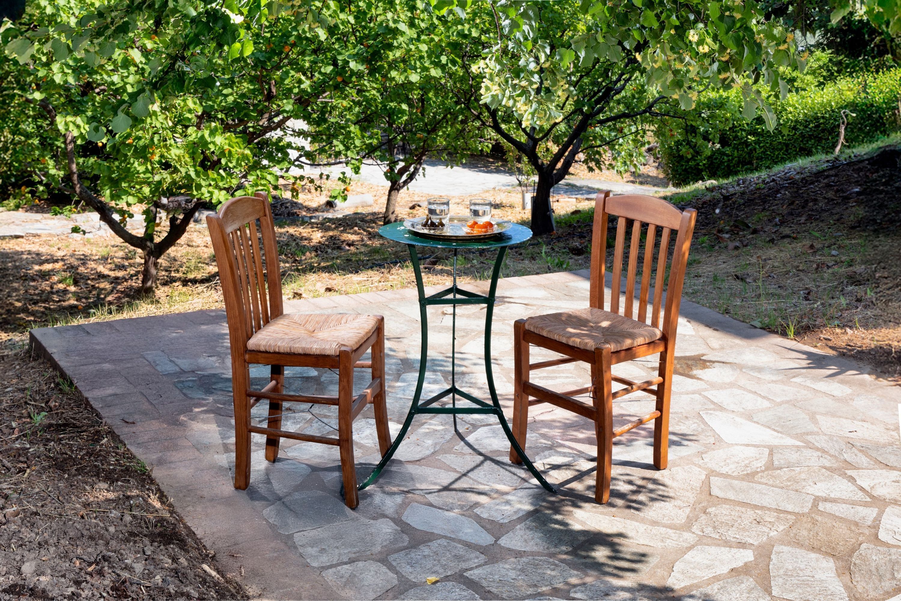 Une terrasse avec deux chaises en bois et une petite table ronde, entourée de dalles de pierre et de verdure.