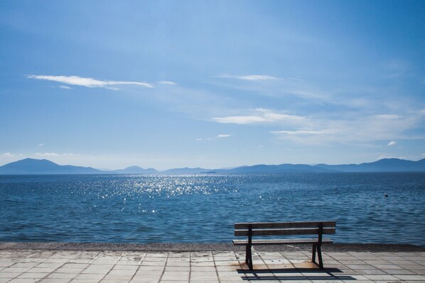 Eine Bank am ruhigen Meer mit Bergen in der Ferne unter klarem Himmel.