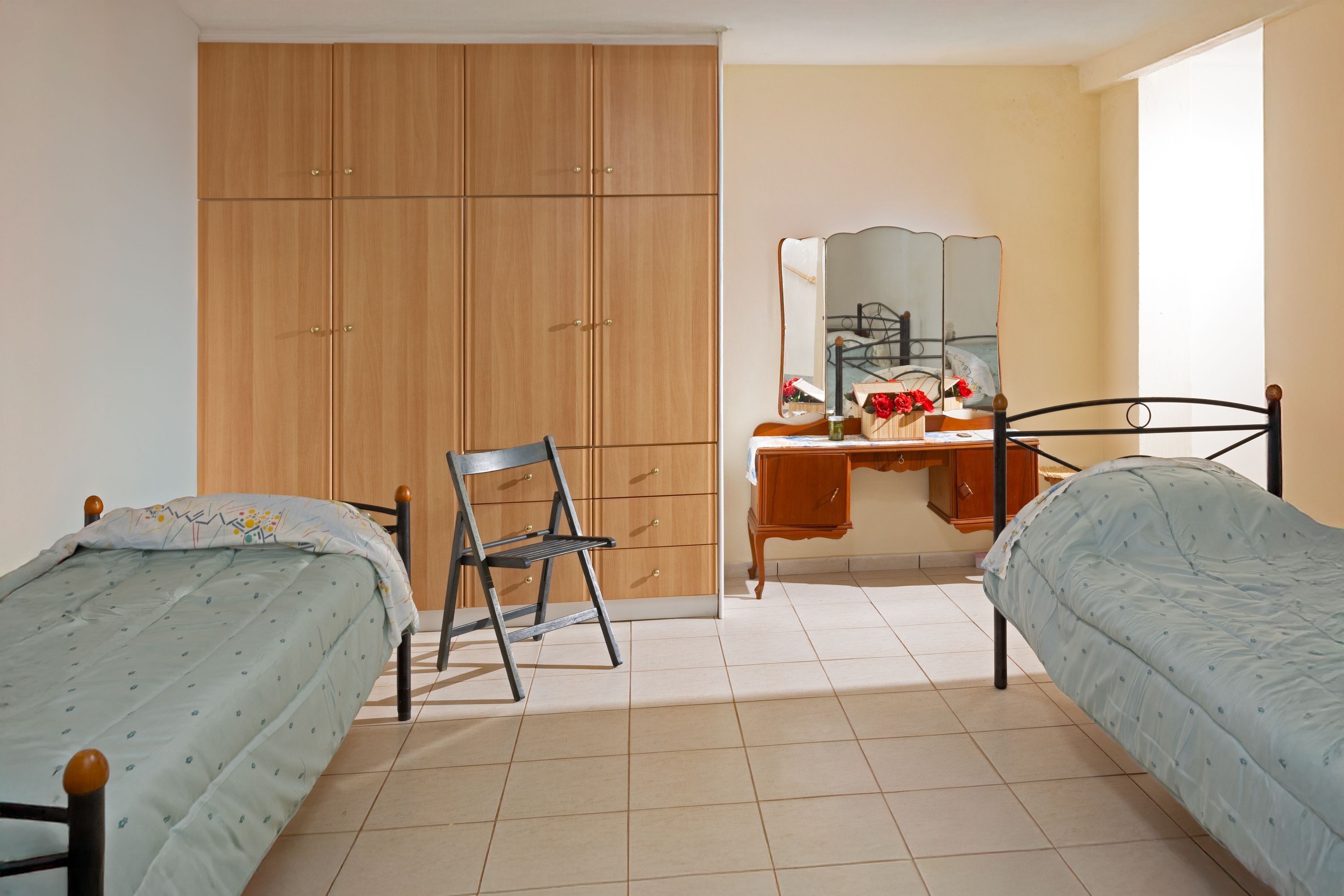 Une chambre avec deux lits simples, une armoire en bois, un bureau avec un miroir et une chaise.