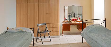 Une chambre avec deux lits simples, une armoire en bois, un bureau avec un miroir et une chaise.