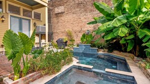 Une piscine entourée d’un mur en briques et de grandes plantes vertes.