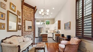 Un salon spacieux avec un canapé, un fauteuil et une table basse, une cuisine à l’arrière-plan et un mur d’accent en briques.