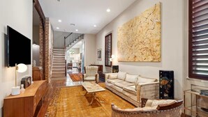 Un salon comprenant un canapé, un fauteuil et une table basse, un téléviseur et un grand tableau abstrait accroché au mur.