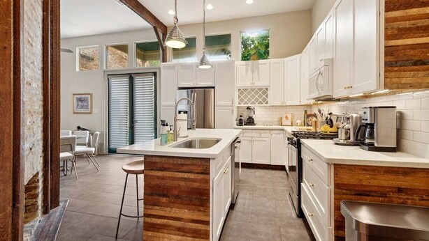 Une cuisine moderne avec des meubles blancs, un îlot central en bois, des appareils électroménagers en acier inoxydable et des luminaires suspendus.