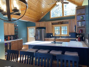 A kitchen with wooden cabinets, a large island with bar stools, a refrigerator, and a ceiling fan.