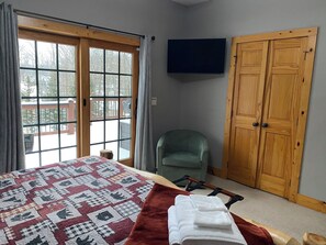 A room with a bed, a chair, a TV, and a wooden door.