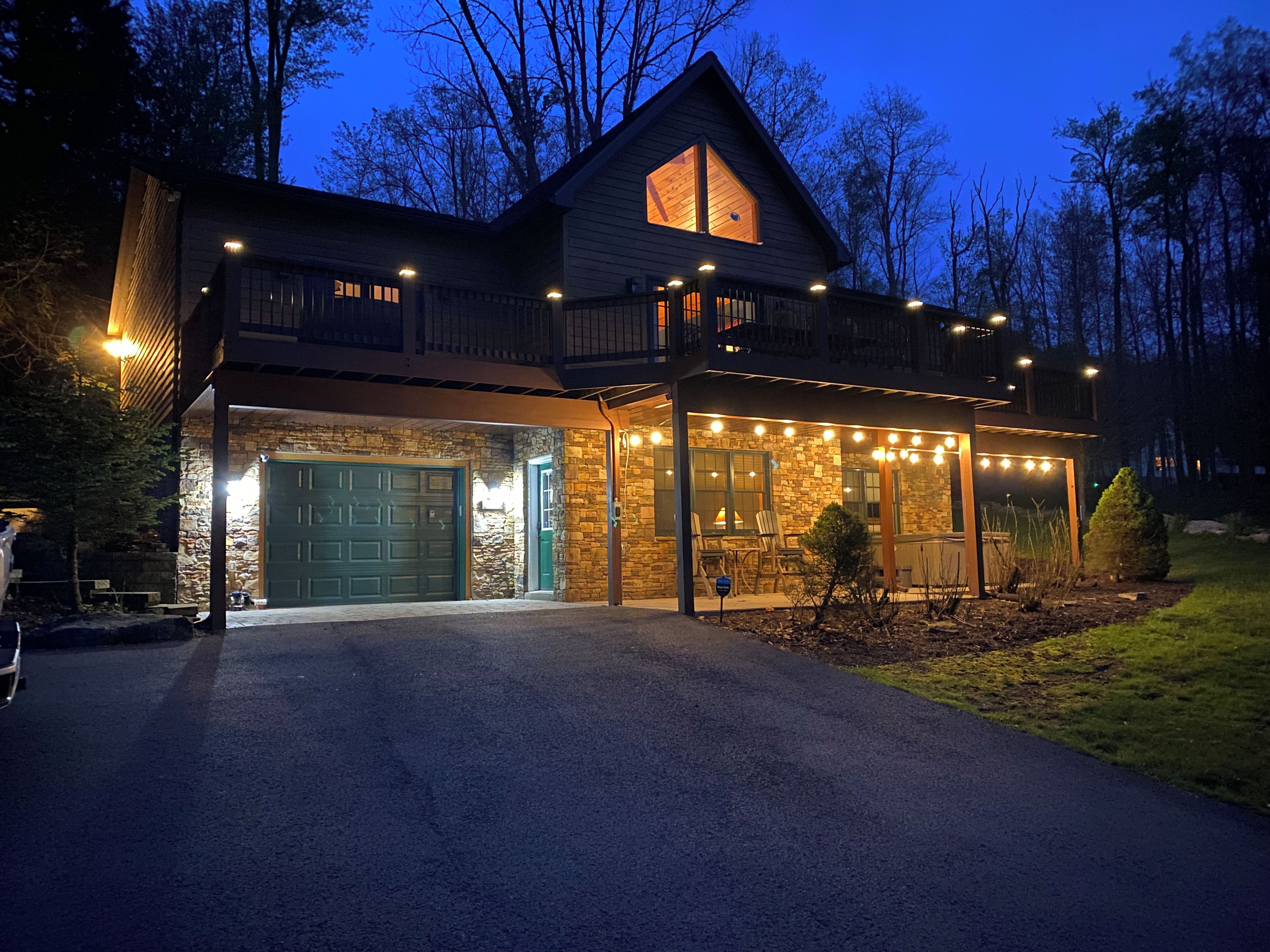 A two-story house with a stone facade, a green garage door, and a balcony with string lights.