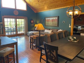 A dining area with a wooden table, chairs, and a bench. There is a sofa and a lamp in the background.