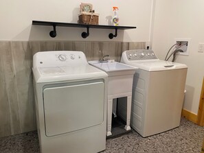 A laundry area with two white washing machines, a sink, and a shelf with a basket and a bottle. - 5 Bedroom in Deep Creek (Oakland)