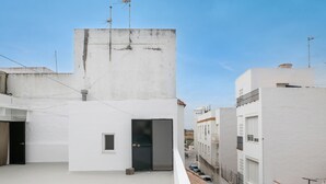 Una azotea con un edificio blanco, una puerta negra y un ventanal pequeño.