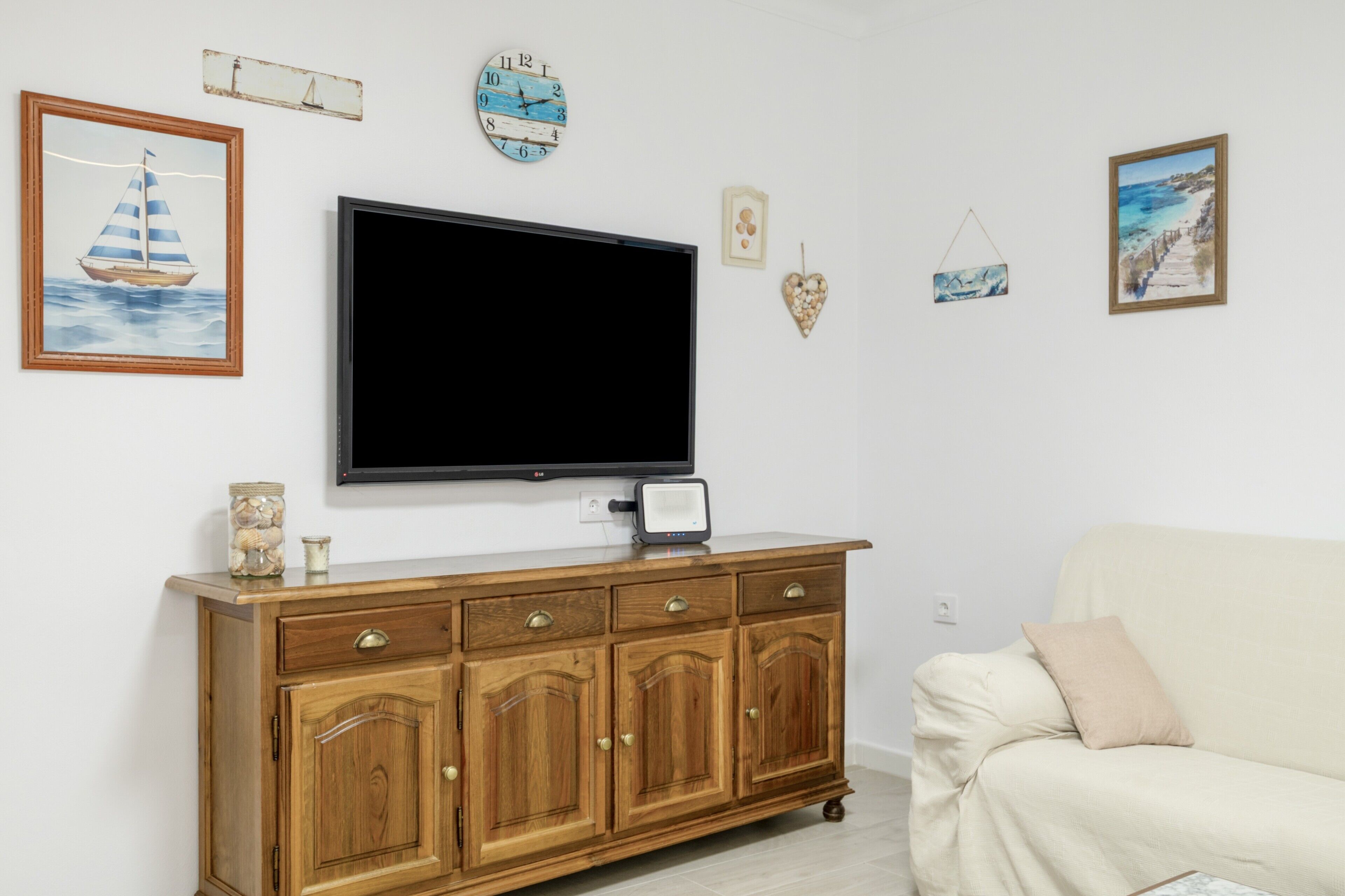 Un salon avec un téléviseur à écran plat, un meuble en bois et un canapé beige.