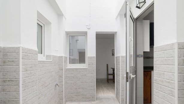 Un pasillo estrecho con paredes de ladrillo blanco, una ventana y una puerta que da a una habitación.