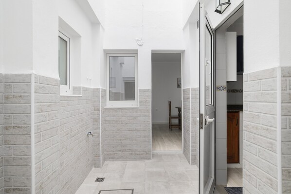 Un couloir étroit aux murs de briques blanches, avec une fenêtre et une porte donnant sur une pièce.