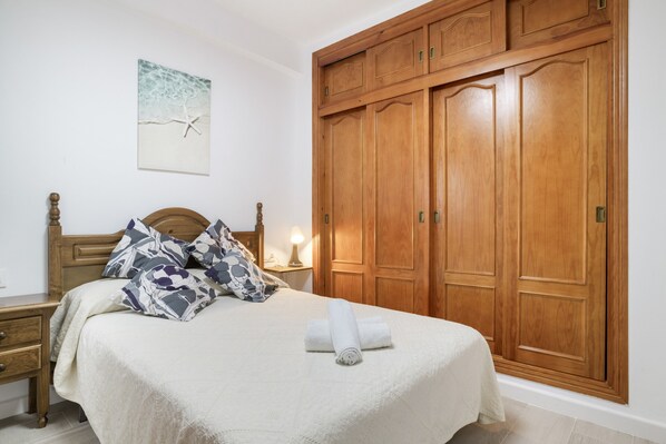 Une chambre à coucher comprenant un lit, une armoire en bois, une table de chevet, une lampe et un tableau mural.