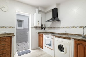 Une cuisine équipée d’un four encastré, d’un lave-vaisselle et d’un lave-linge, avec une fenêtre et une horloge au mur.