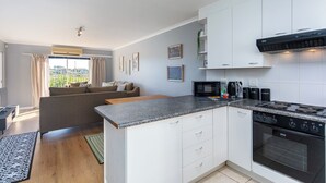 Ett modernt kök med vita skåp, en bänkskiva i granit och en svart spis. Det finns ett fönster med gardiner och utsikt över grönområden utanför.