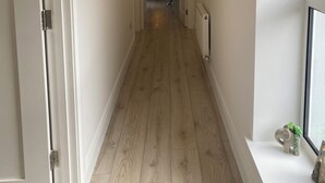 Un couloir étroit avec un plancher en bois, des murs blancs et une porte sur le côté gauche.