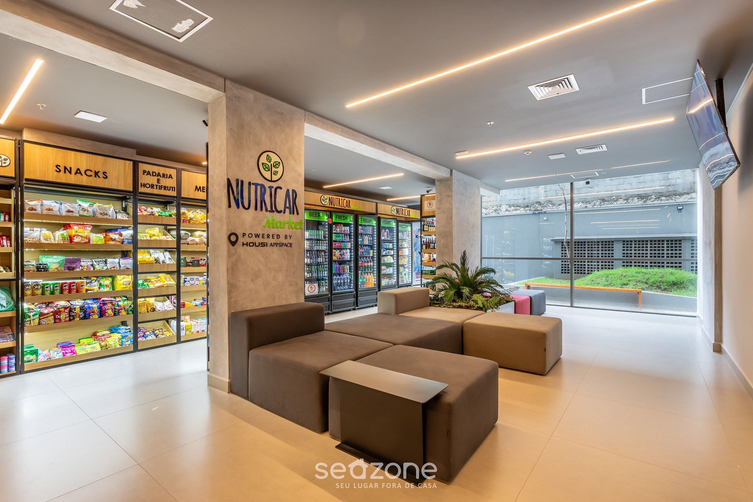 Um interior moderno com áreas de estar, prateleiras para lanches e expositores refrigerados para bebidas.