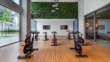 Uma academia com bicicletas ergométricas, piso de madeira, parede verde e grandes janelas.