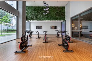 A gym with stationary bikes, a wooden floor, a green wall, and large windows.
