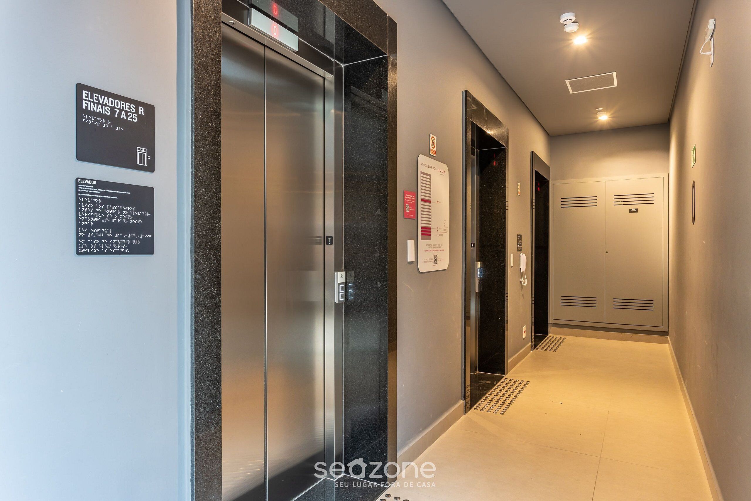 Um elevador moderno com mostrador digital, placa indicando o andar de destino e aviso de segurança contra incêndio fixado na parede.