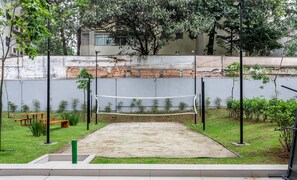 A tennis court with a net, surrounded by a low wall and greenery.