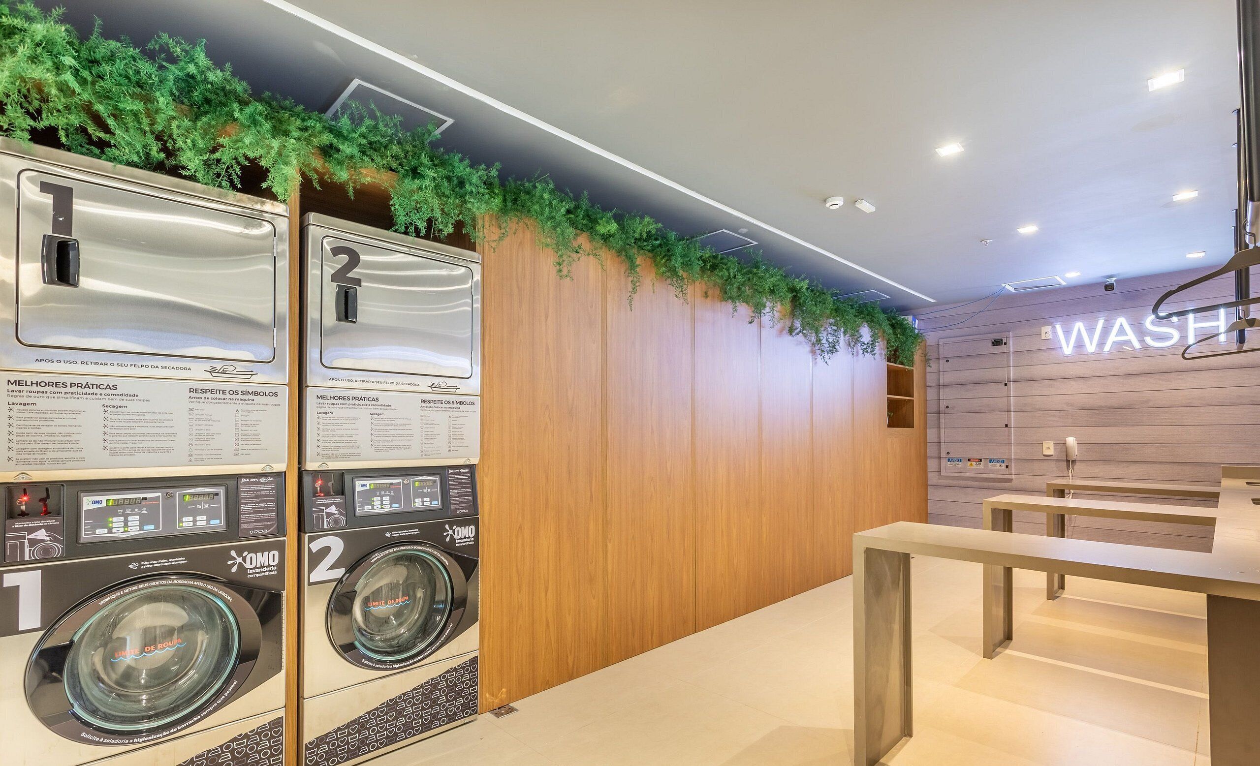 Un moderno cuarto de lavandería con dos lavadoras, paredes de madera e instalación de plantas verdes.