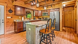 A kitchen with wooden cabinets, a granite countertop, a refrigerator, and a bar stool. - Oakmont Lodge: 8 acres•HotTub•free tkts•pool table (Gatlinburg)