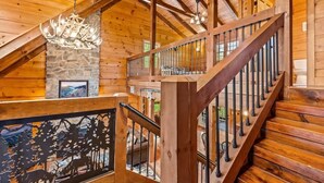 A wooden staircase with a railing, a chandelier, and a stone wall. - Oakmont Lodge: 8 acres•HotTub•free tkts•pool table (Gatlinburg)