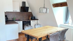 A modern kitchen with a wooden dining table and chairs, a hanging light fixture, and a view of the outside through a window. - Vacation apartment Minkwitz in the nursery house in Fürstlich Drehna (Luckau, OT Fürstlich Drehna)
