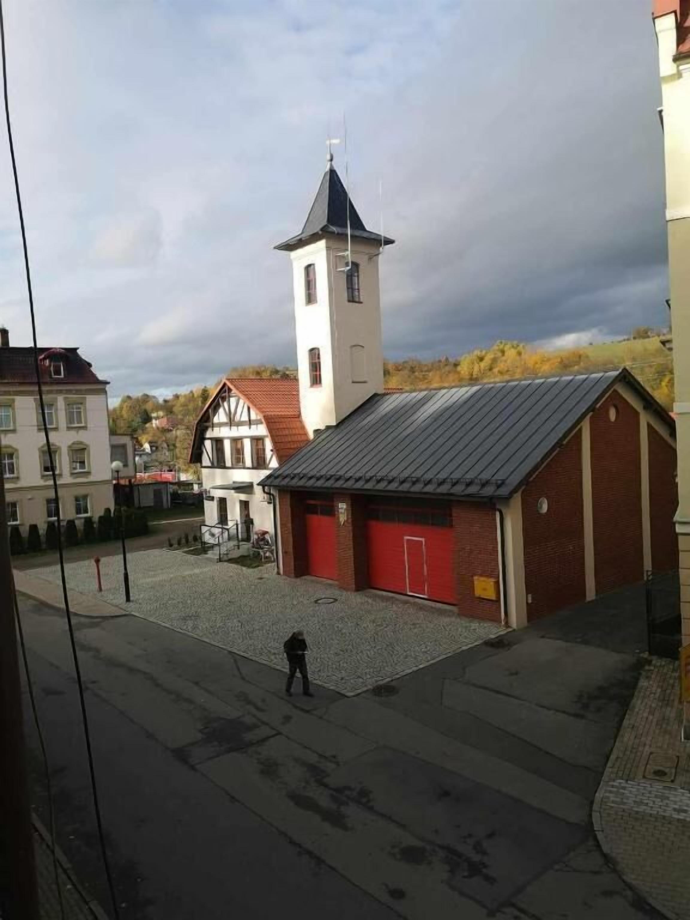 Un edificio con puerta de garaje roja, una torre blanca y una persona caminando al frente.