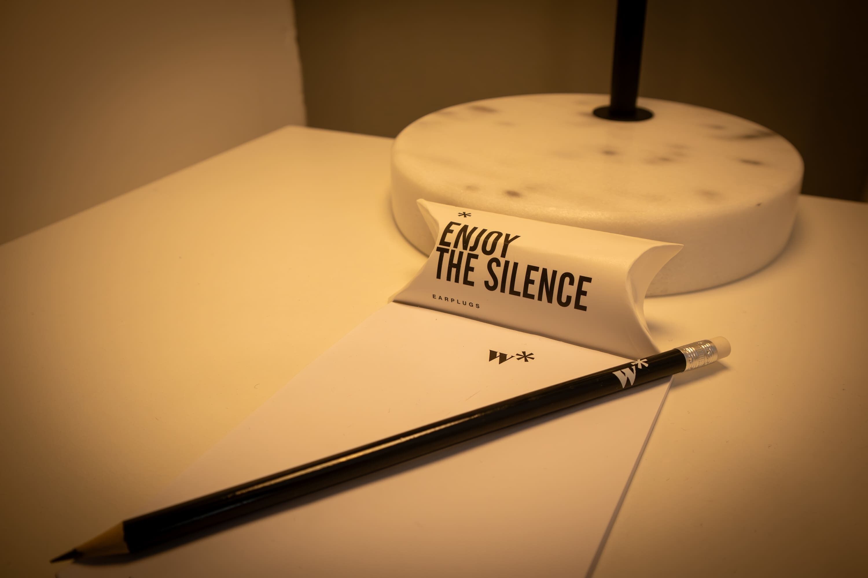 Un bureau blanc avec un stylo noir, une feuille de papier blanche sur laquelle est écrit « PROFITEZ DU SILENCE », et un objet blanc doté d’un manche noir.