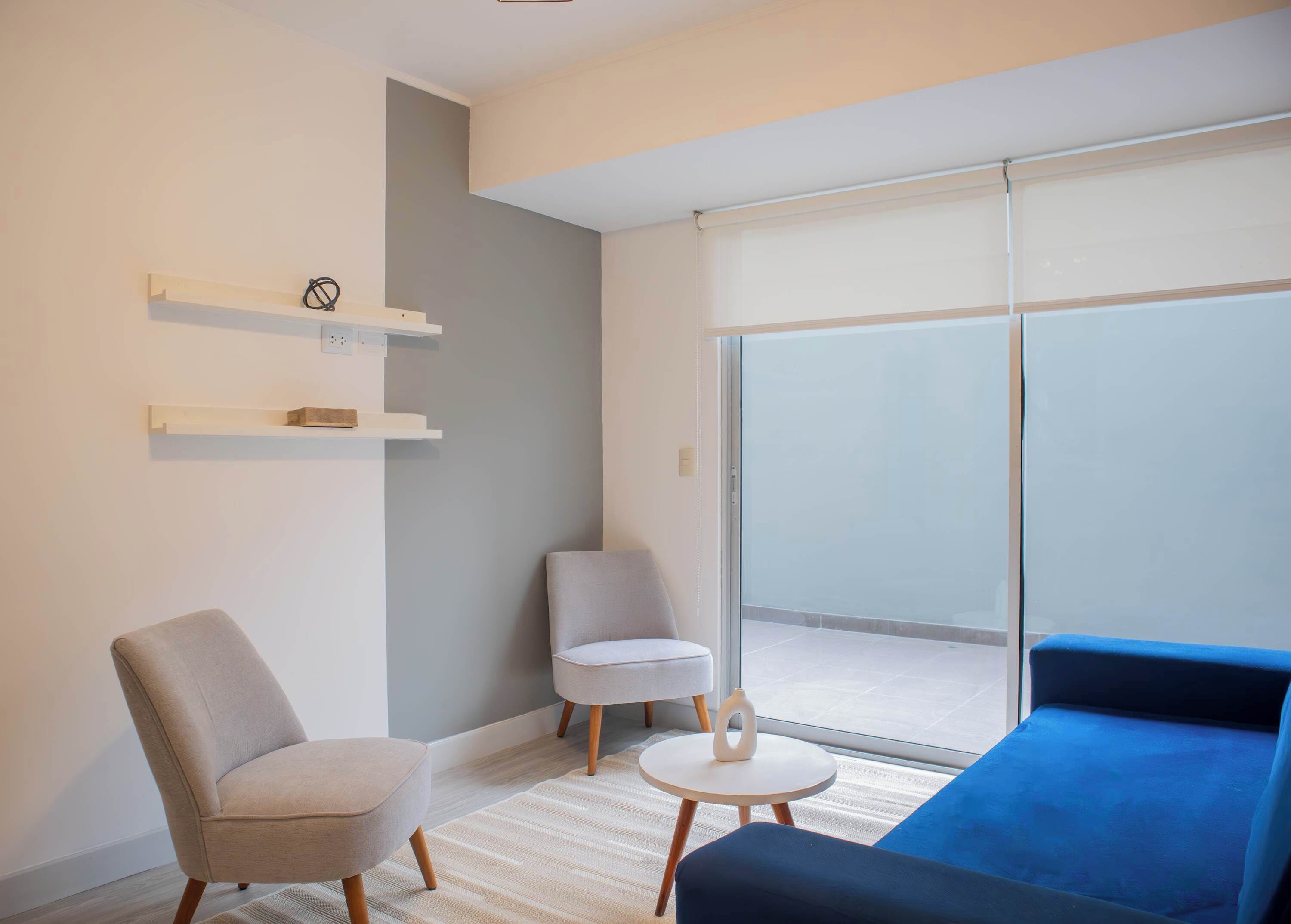 Un salon moderne comprenant un canapé, deux fauteuils, une petite table et une porte-fenêtre coulissante donnant sur un balcon.