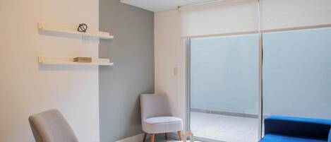 Un salon moderne comprenant un canapé, deux fauteuils, une petite table et une porte-fenêtre coulissante donnant sur un balcon.