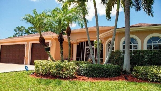 A residential house with a garage, palm trees, and a well-maintained lawn.