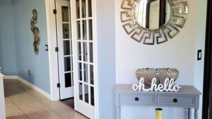 A hallway with a light blue wall, a decorative mirror, a console table with a 'hello' sign, and a yellow vase.