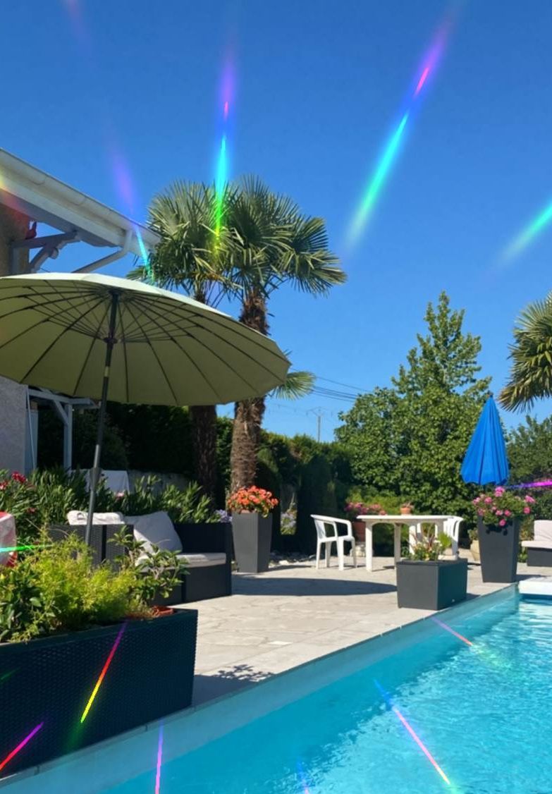 Een zwembad met een terras, inclusief een tafel en stoelen, omgeven door planten en parasols.