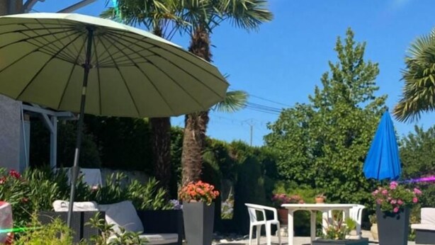 A swimming pool with a patio area, including a table and chairs, surrounded by plants and umbrellas. - Mimosa room - Domaine de la Provençale (ST DIDIER DE LA TOUR)