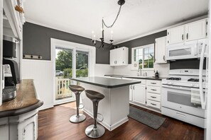 A modern kitchen with white cabinets, a central island with stools, a chandelier, and a view through the glass doors.