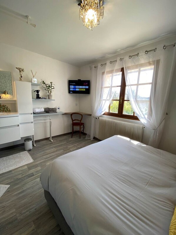 Un dormitorio con una cama grande, un escritorio con silla, un televisor y una ventana con cortinas.