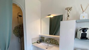 Une salle de bain moderne avec un meuble-lavabo blanc, un grand miroir, une douche et une petite plante.