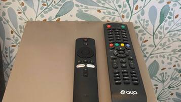 En stikkontakt på væggen med to USB-porte, en fjernbetjening og en TV-fjernbetjening på et bord foran blomstret tapet.
