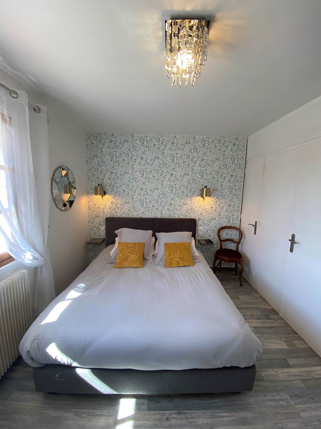 Un dormitorio con cama, dos apliques, un radiador, una silla y una puerta.