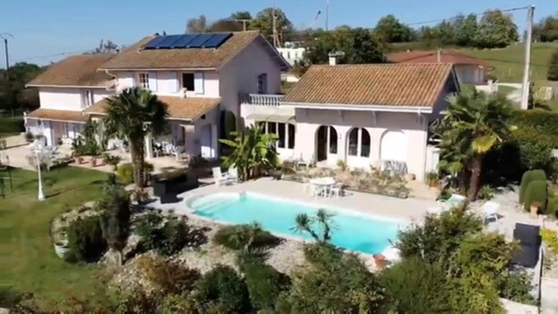Une maison à deux étages dotée d’une piscine, de panneaux solaires et d’un jardin bien entretenu.