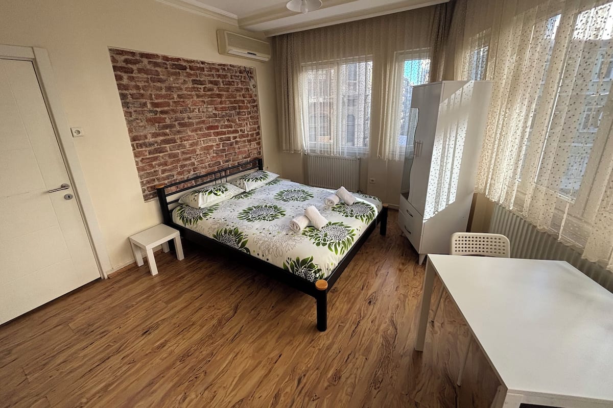 A bedroom with a brick wall, a bed with floral bedding, a desk, and a chair.